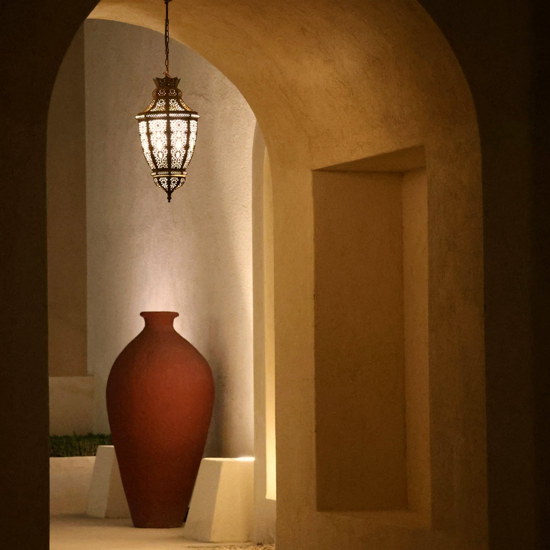 A terracotta urn glowing under a lantern in a warm plaster archway